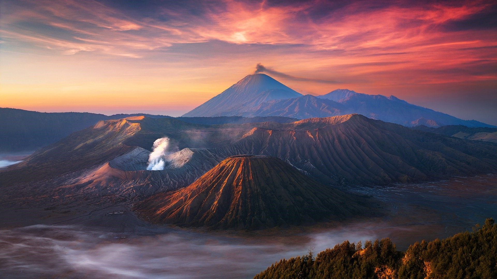 Kaldera Tengger saat matahari terbit: Bromo mengepul, Batok di sampingnya, Semeru di kejauhan, dan awan memenuhi dasar kaldera.